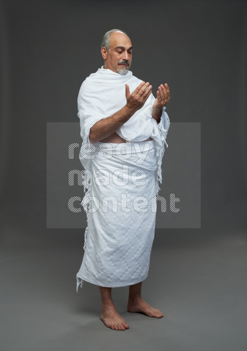A man wearing Ehram Standing dua'a on gray background