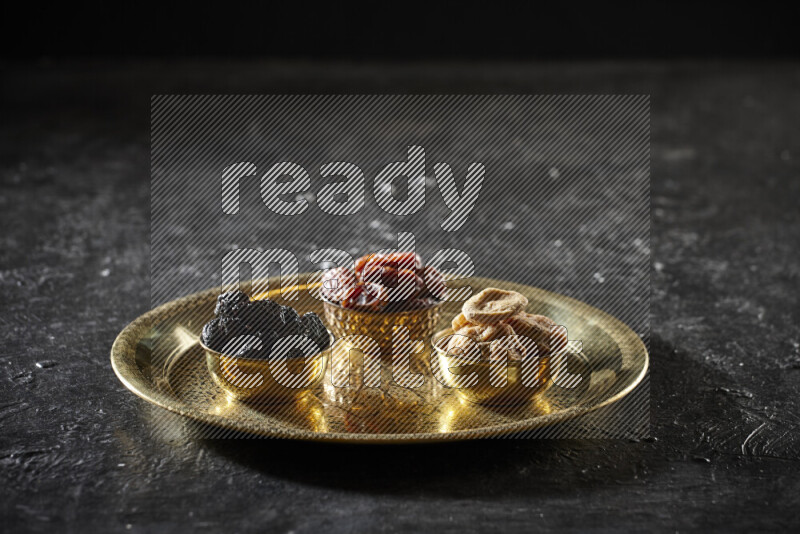 Dried fruits in metal bowls on a tray in a dark setup