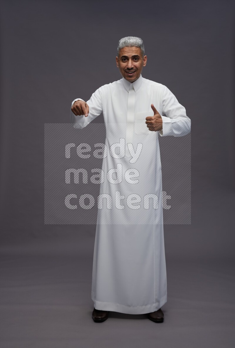 Saudi man wearing thob standing interacting with the camera on gray background