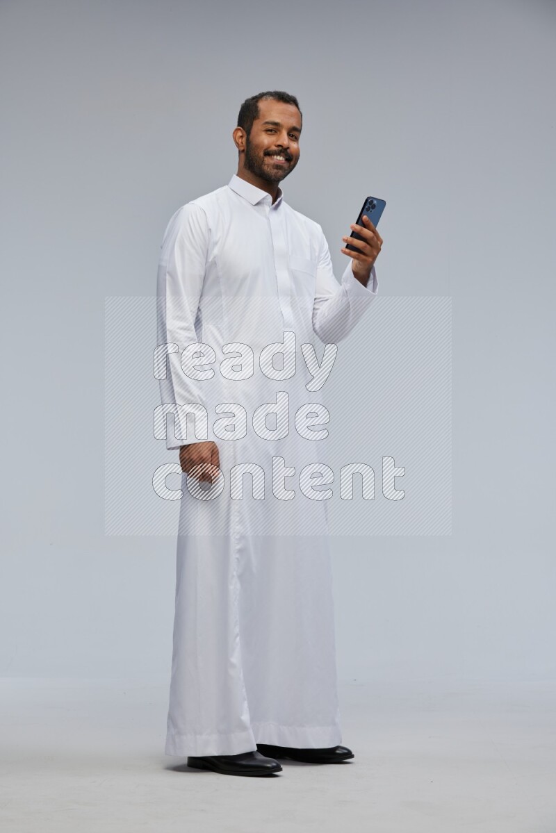 Saudi man wearing Thob standing texting on phone on Gray background