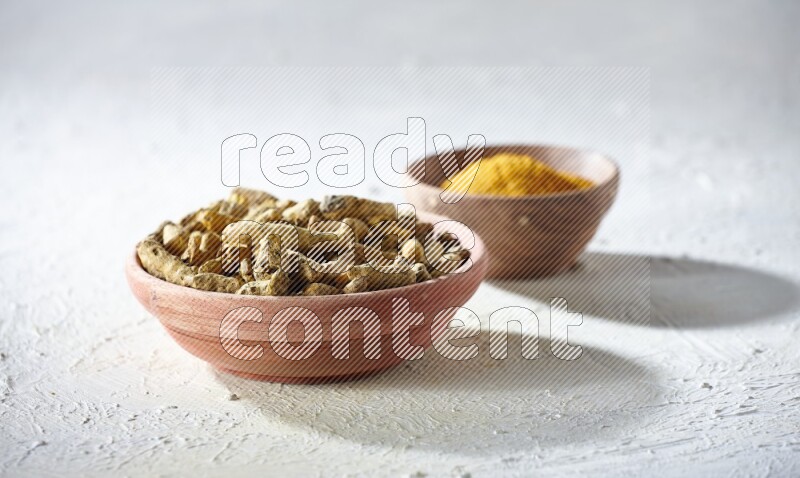 وعاءان خشبيان، أحدهما ممتلئ ببودرة الكركم والآخر بأصابع الكركم المجففة، على خلفية بيضاء