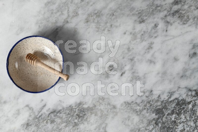 Multicolored pottery bowl with wooden honey dipper in it on grey marble background