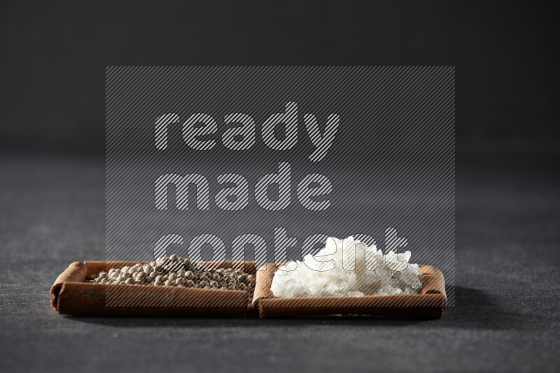 مربعان من أعواد القرفة ممتلئان بحبوب الفلفل الأسود والملح علي خلفية سوداء