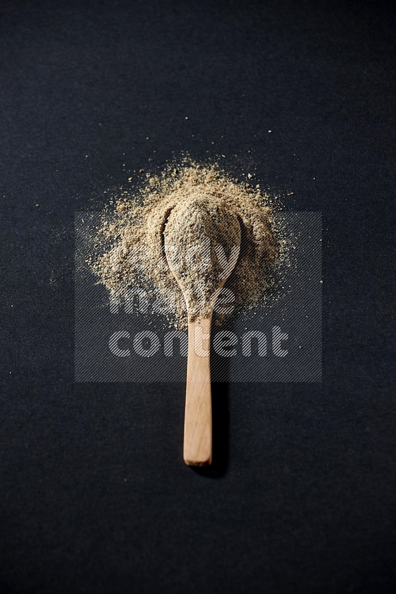A wooden spoon full of cardamom powder and powder spreaded on black flooring
