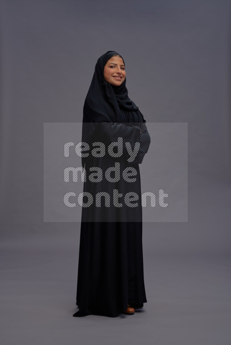 Saudi woman wearing Abaya standing with crossed arms on gray background