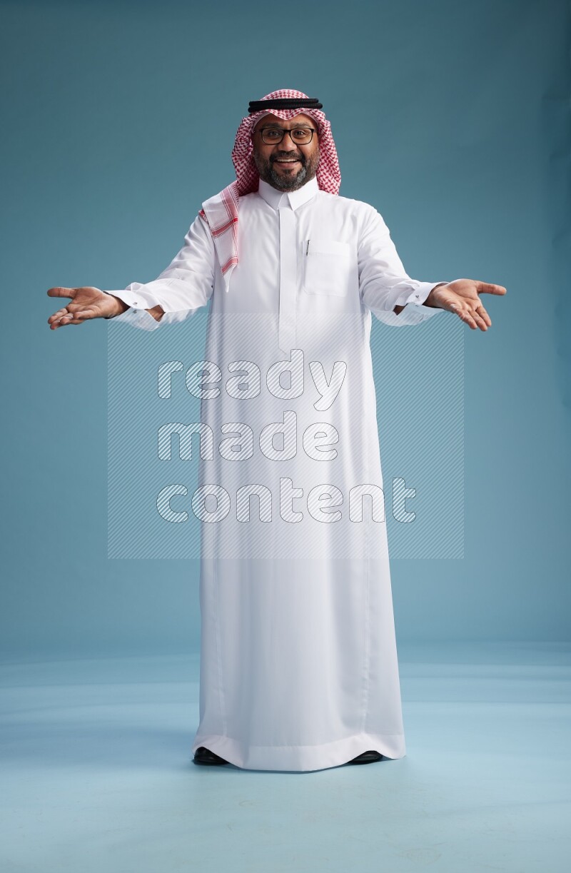 Saudi Man with shimag Standing Interacting with the camera on blue background