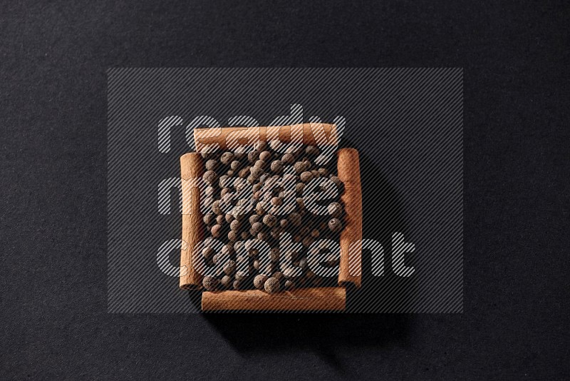 A single square of cinnamon sticks full of allspice on black flooring