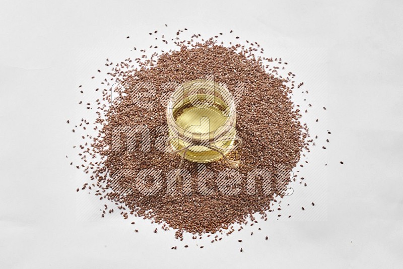 A glass jar full of flax oil surrounded by flax seeds on a white flooring in different angles