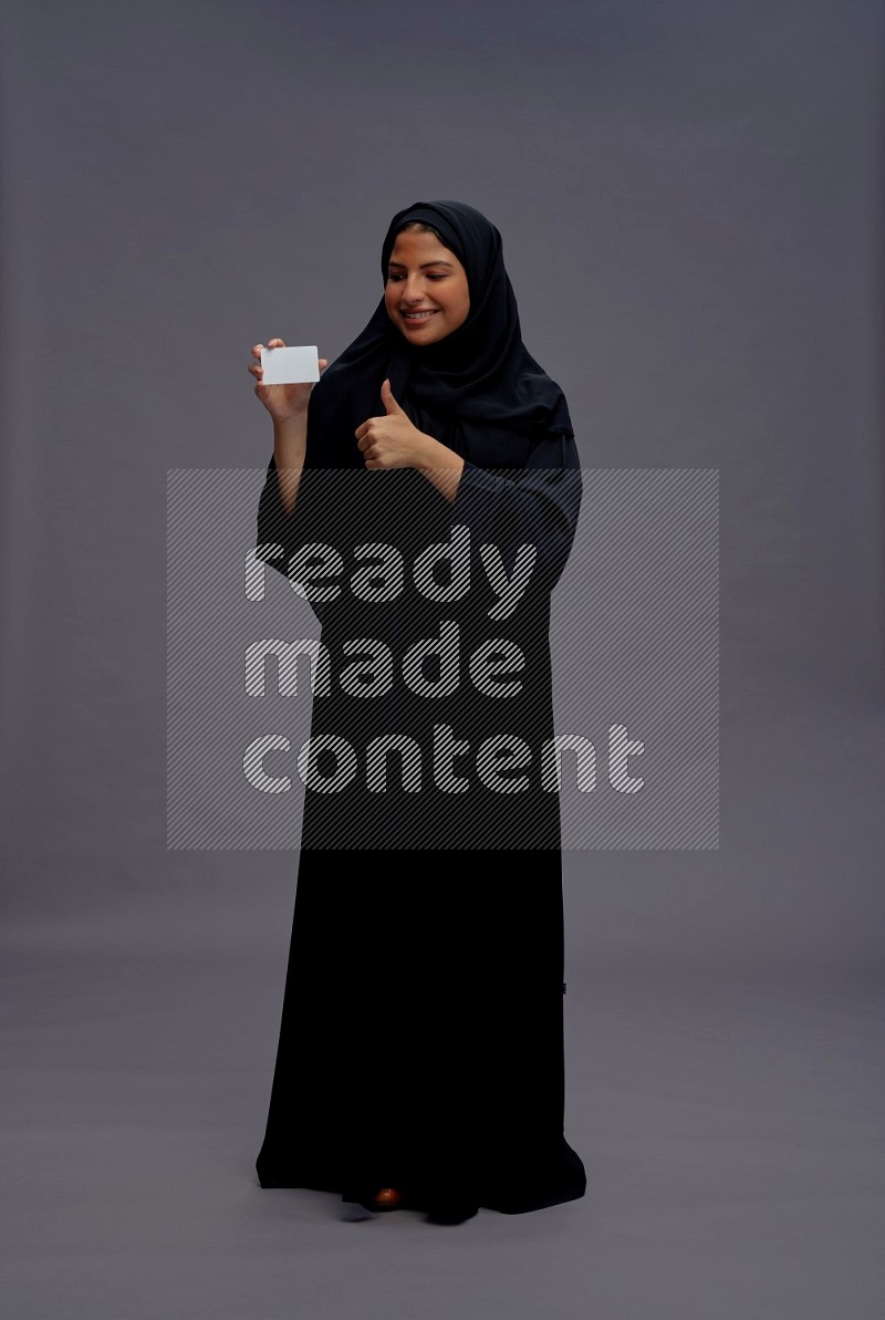 Saudi woman wearing Abaya standing holding ATM card on gray background