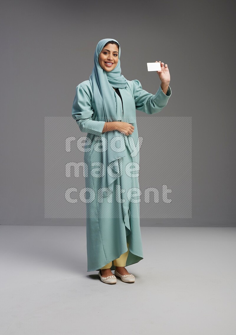 Saudi Woman wearing Abaya standing holding ATM card on Gray background