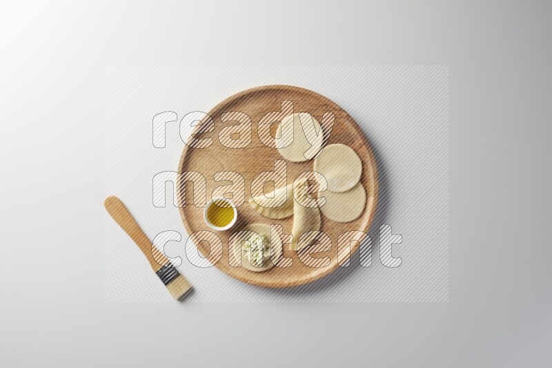 two closed sambosas and one open sambosa filled with cheese while oil with oil brush aside in a wooden dish on a white background