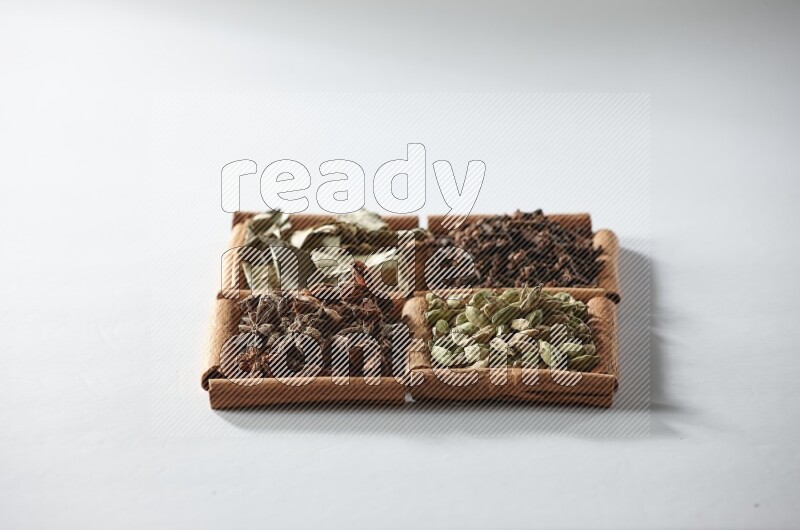 4 مربعات من أعواد القرفة ممتلئة بالهيل واليانسون والقرنفل وأوراق الغار على أرضية بيضاء