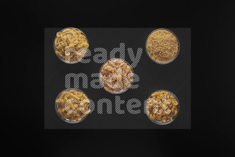 Different pasta types in 5 glass bowls on black background