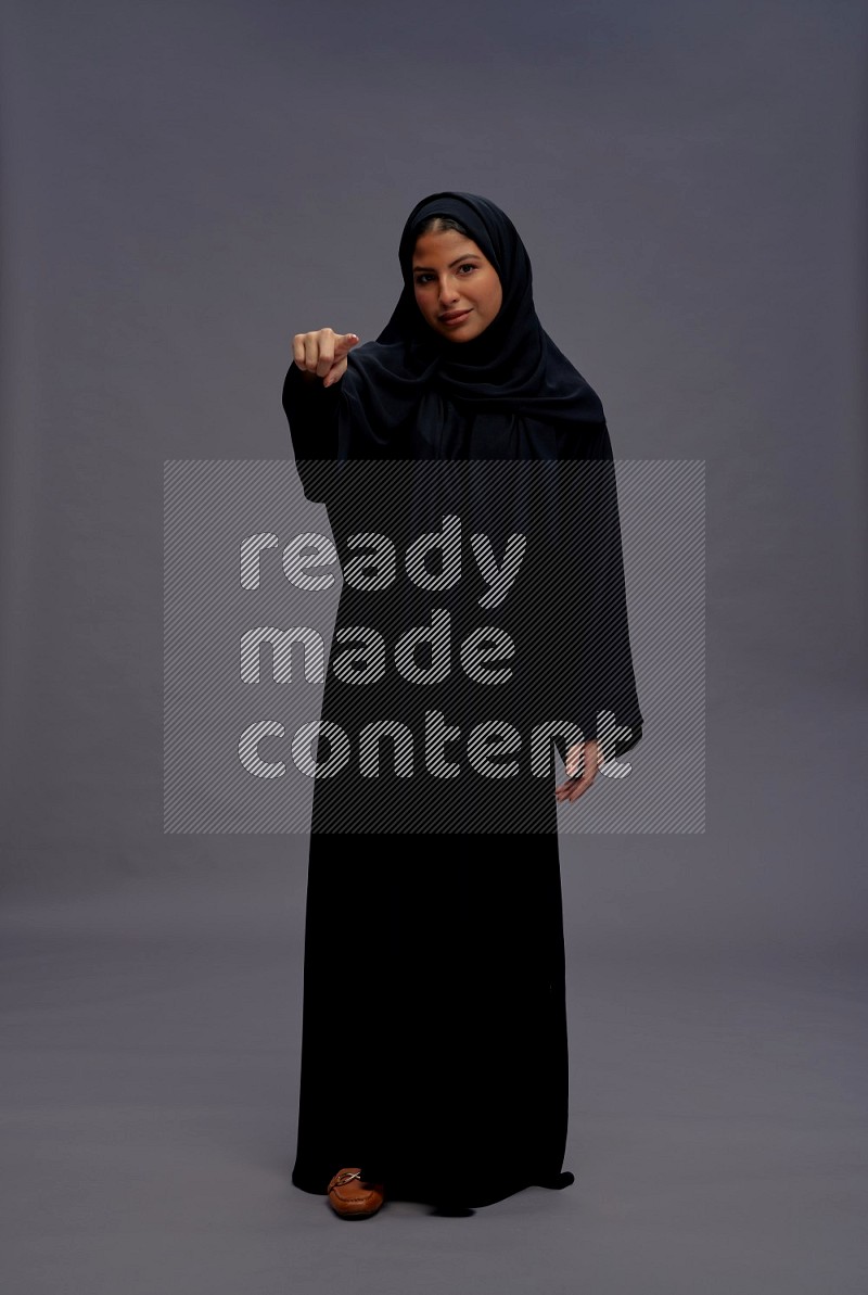 Saudi woman wearing Abaya standing interacting with the camera on gray background