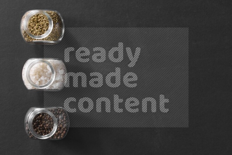 ملح والفلفل الأسود والكمون في أوعية زجاجية علي خلفية سوداء