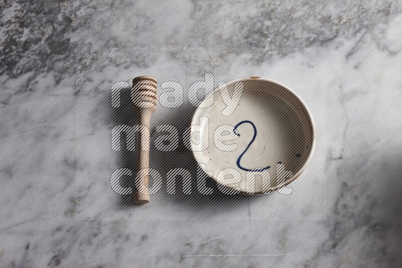Multicolored pottery bowl with wooden honey dipper on the side on grey marble background