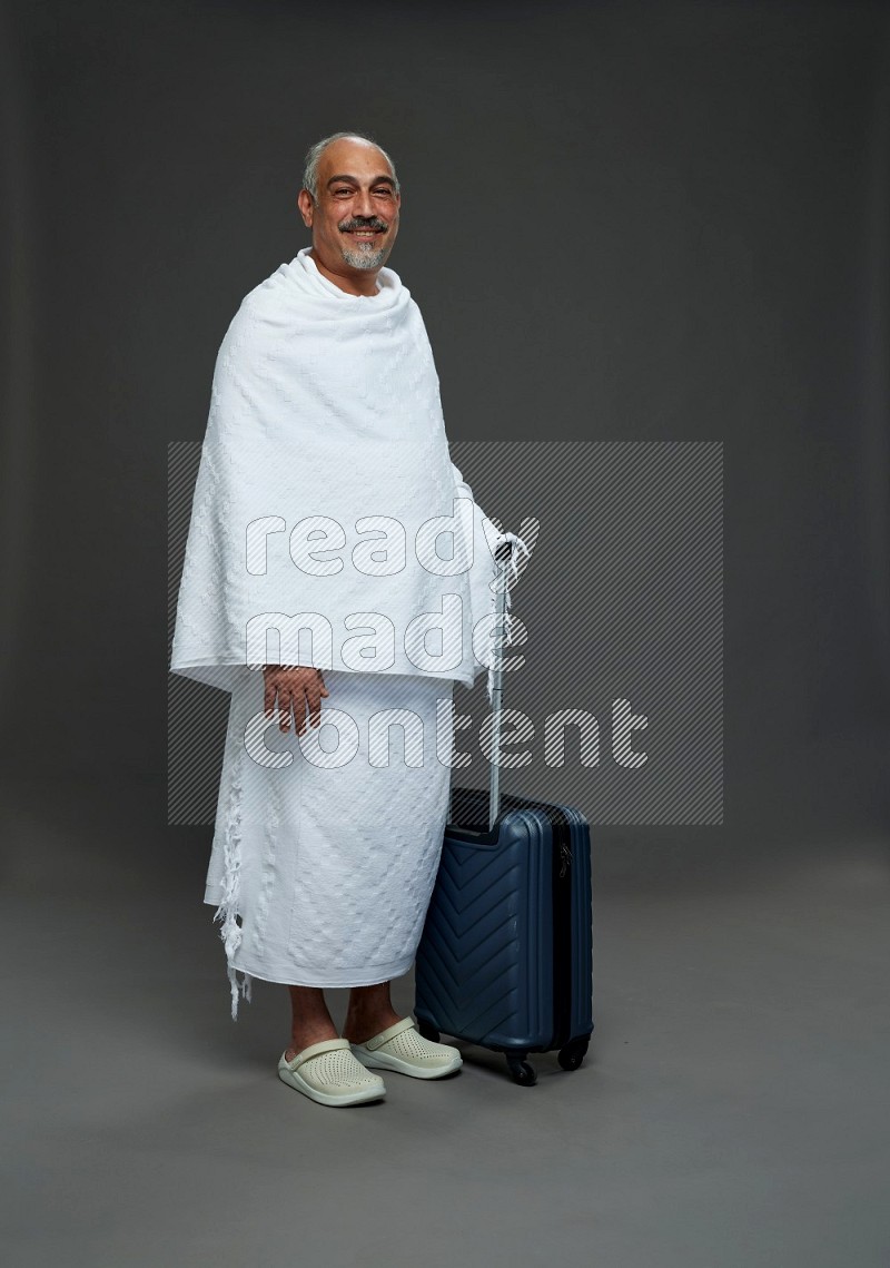 A man wearing Ehram Standing holding traveling bag on gray background