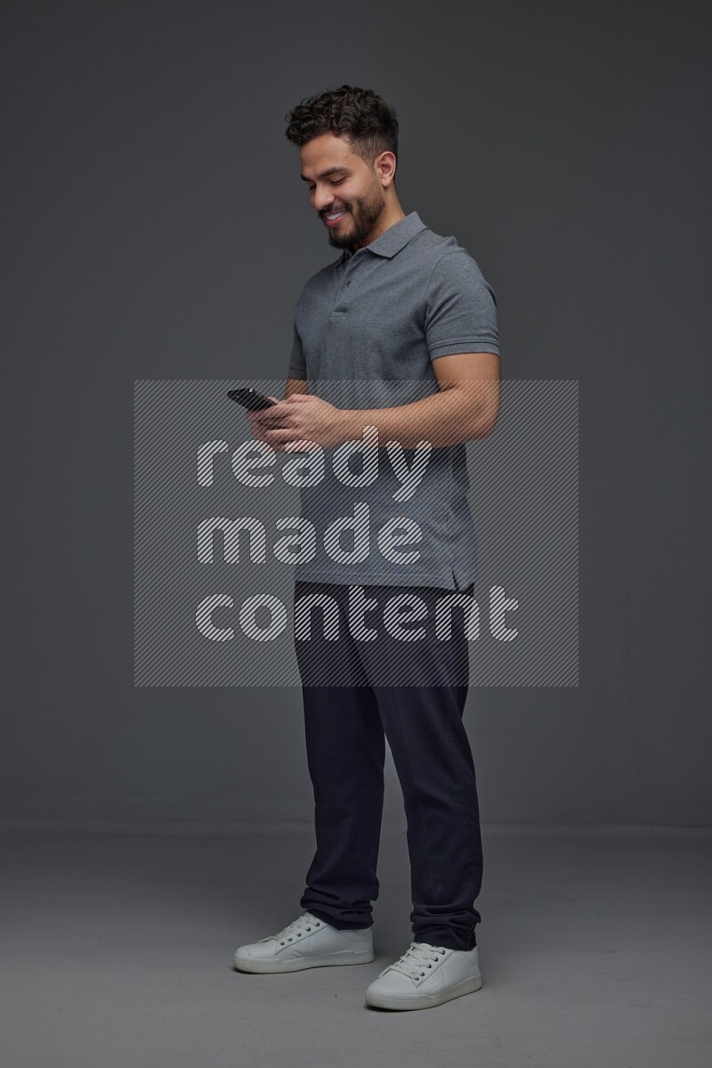 A man wearing casual standing and using his phone eye level on a gray background