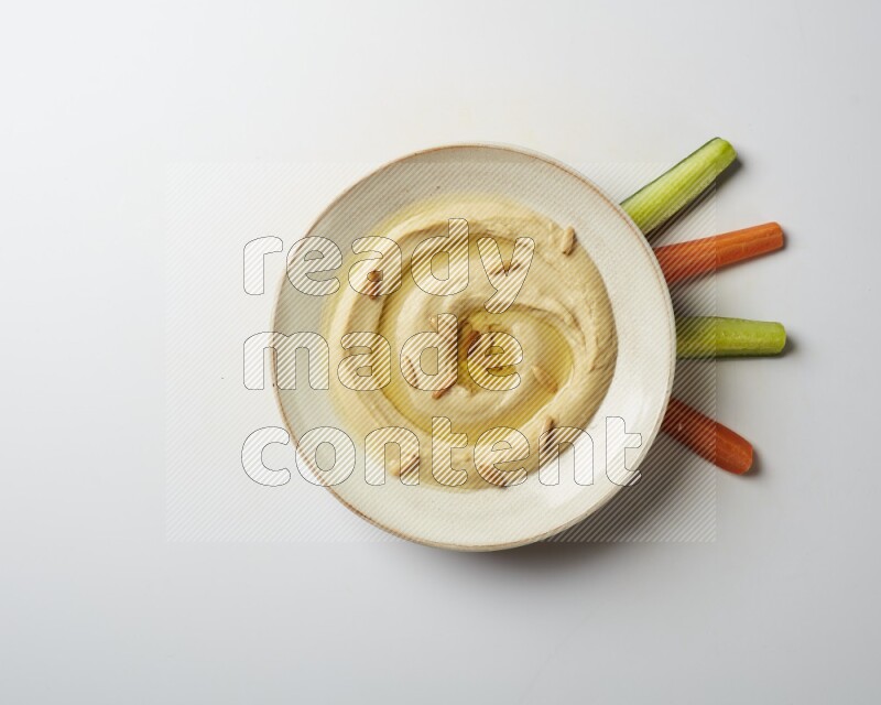 Hummus in a pottry plate garnished with pine nuts on a white background