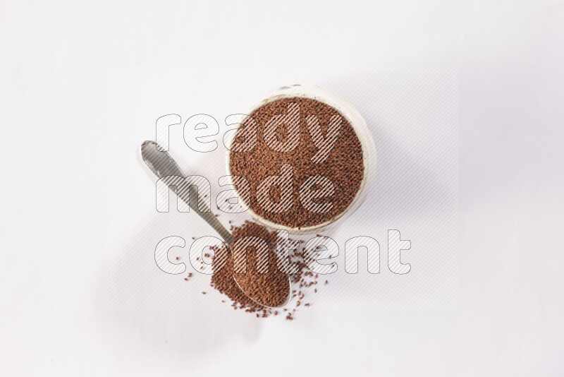 A beige pottery bowl and a metal spoon full of garden cress seeds on a white flooring