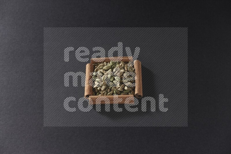 أربعة من أعواد القرفة مكونة شكل مربع بداخلها حبوب الهيل علي خلفية سوداء