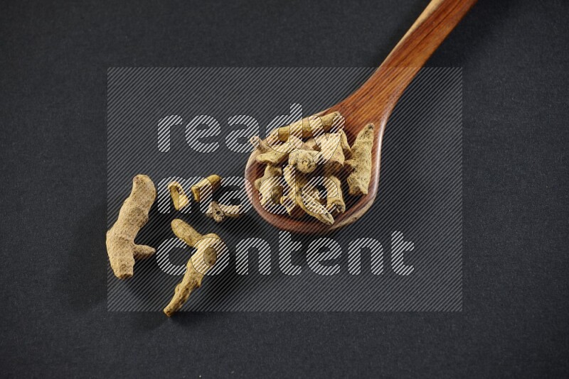 مغرفة خشبية ممتلئة بأصابع الكركم المجففة على خلفية سوداء