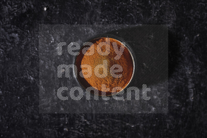 A black pottery bowl full of ground paprika powder on black background