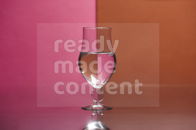 The image features a clear glassware filled with water, set against pink and dark orange background