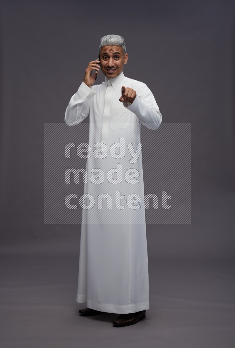 Saudi man wearing thob standing talking on phone on gray background
