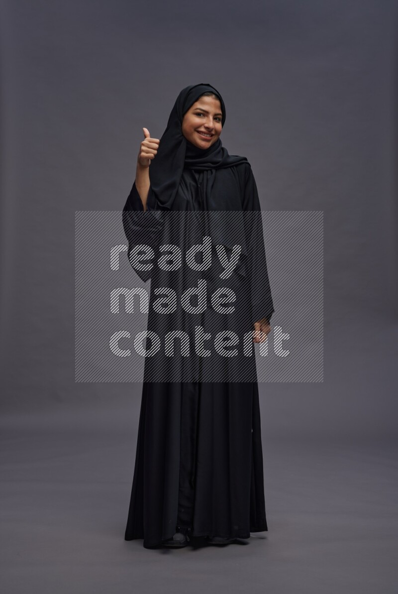 Saudi woman wearing Abaya standing interacting with the camera on gray background