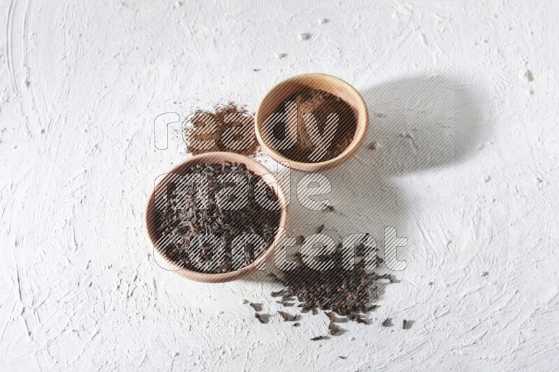 2 wooden bowls full of cloves powder and whole cloves on a textured white flooring