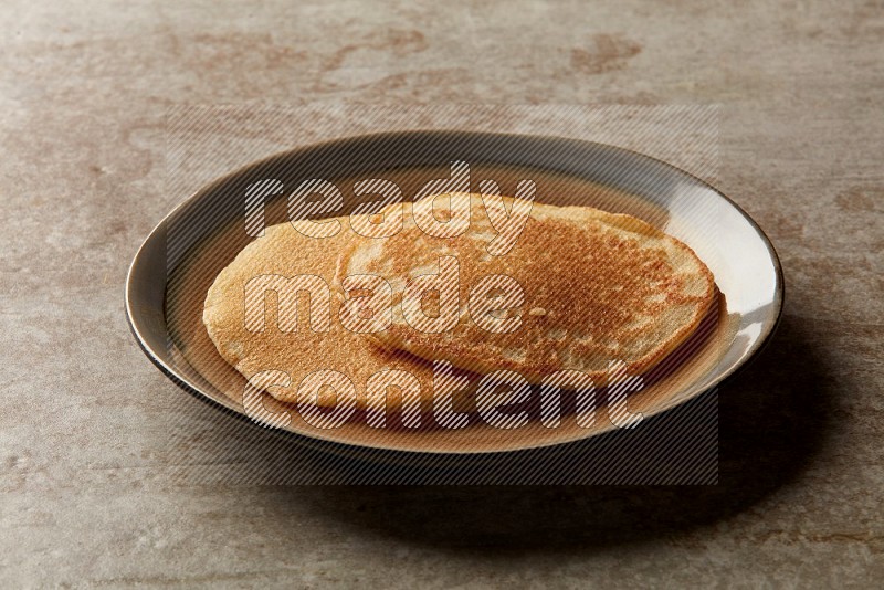 Two stacked plain pancakes in a bicolor plate on beige background