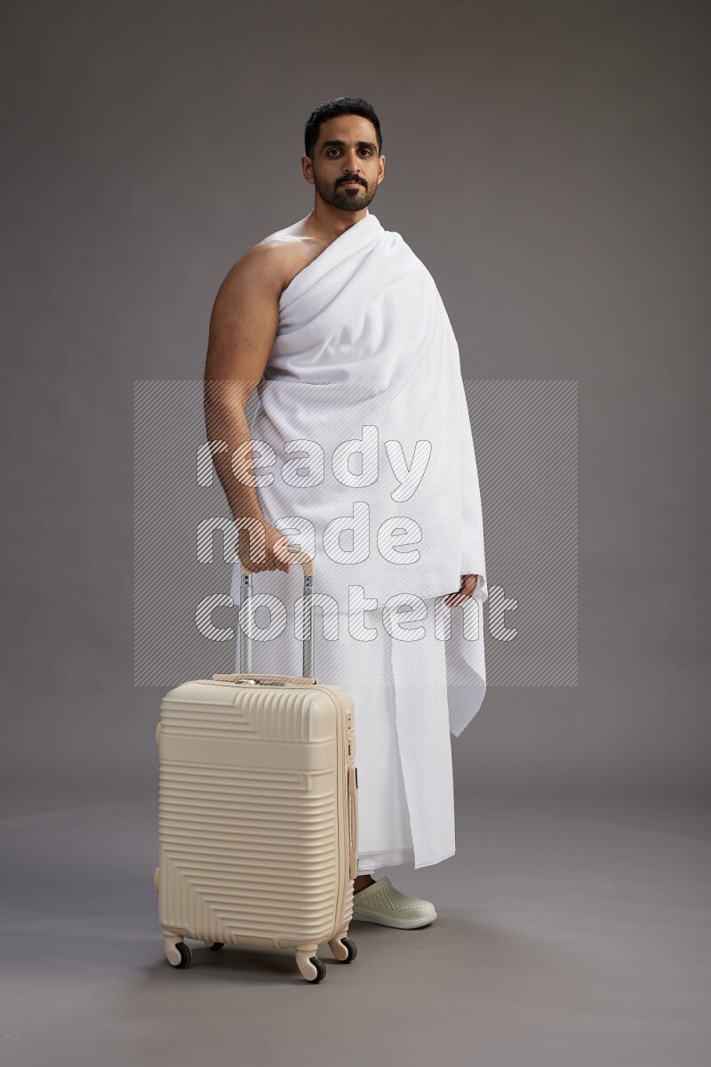 A man wearing Ehram Standing holding traveling bag on gray background