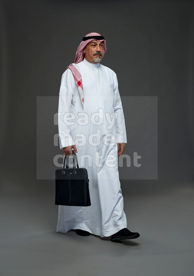 Saudi man with shomag Standing holding bag on gray background