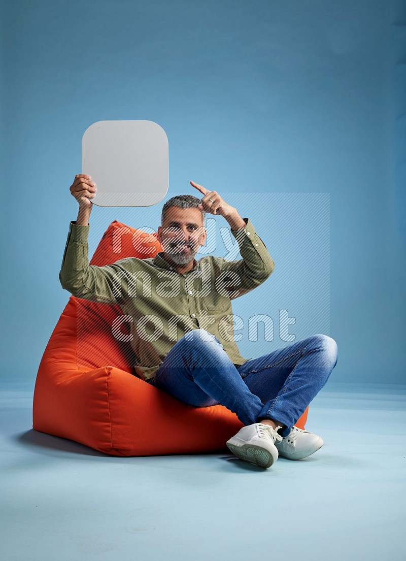 A man sitting on a orange beanbag and holding social media sign