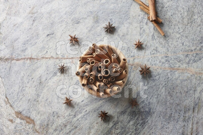 wooden bowl full of cinnamon sticks surrounded by star anis on marble background in different angles