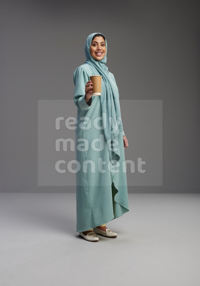 Saudi Woman wearing Abaya standing  holding paper cup on Gray background