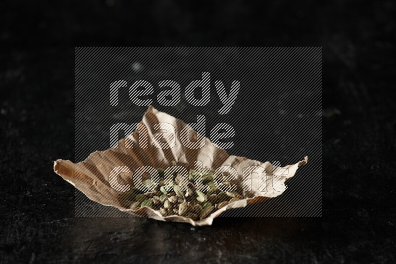 Cardamom seeds in a crumpled piece of paper on textured black flooring