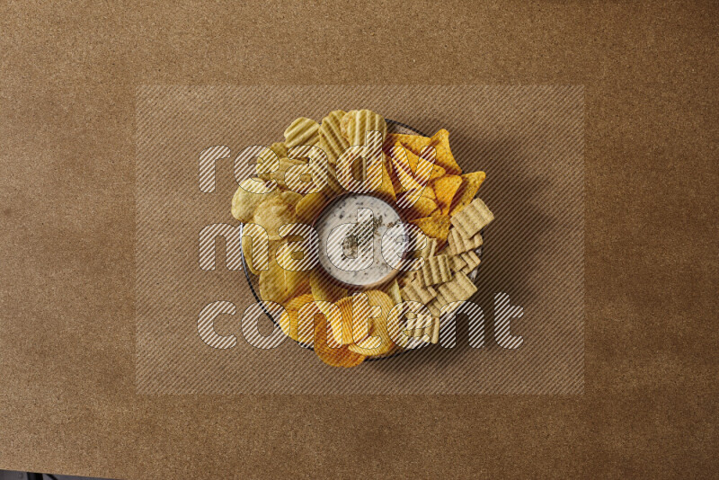 Assorted snacks on a pottery plate with a dipping on brown background