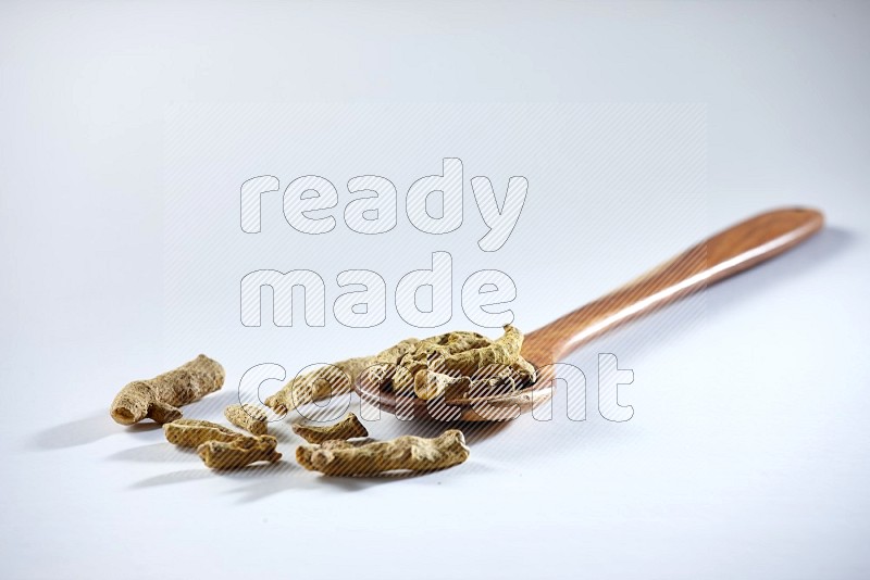 A wooden ladle full of dried turmeric fingers on white flooring