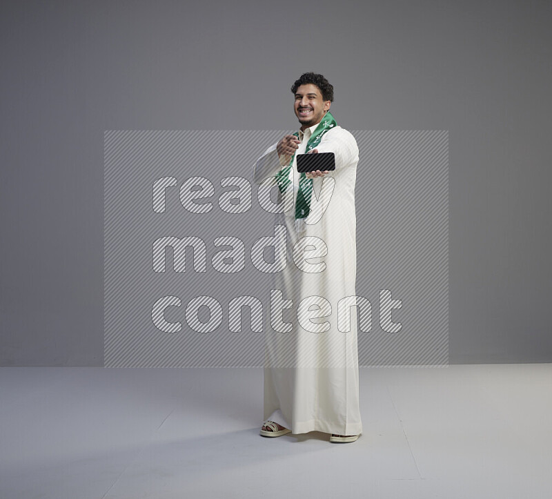 رجل سعودي يرتدي ثوب ابيض و شال يحمل جوال