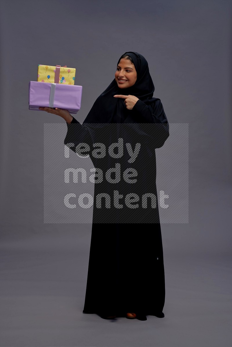 Saudi woman wearing Abaya standing holding gift box on gray background
