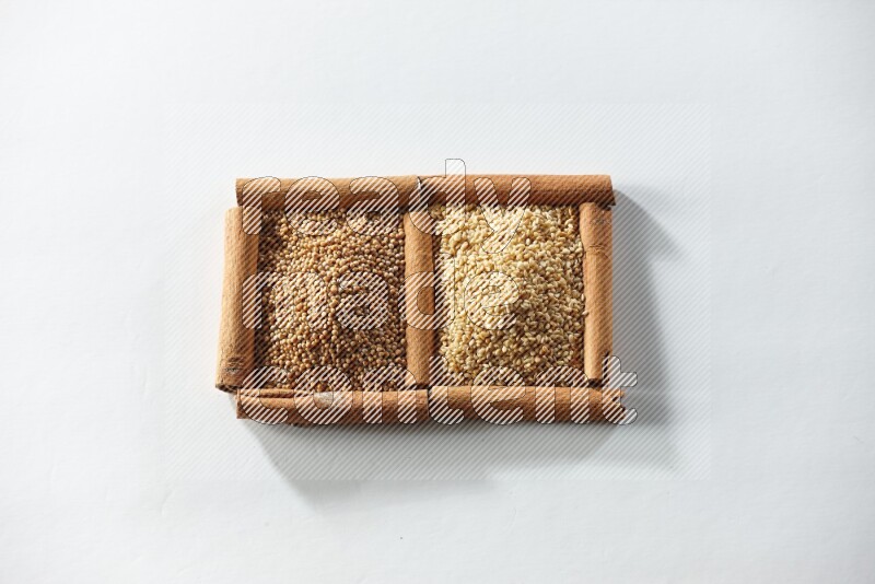 مربعان من أعواد القرفة ممتلئان بحبوب الخردل وبذور السمسم علي خلفية بيضاء