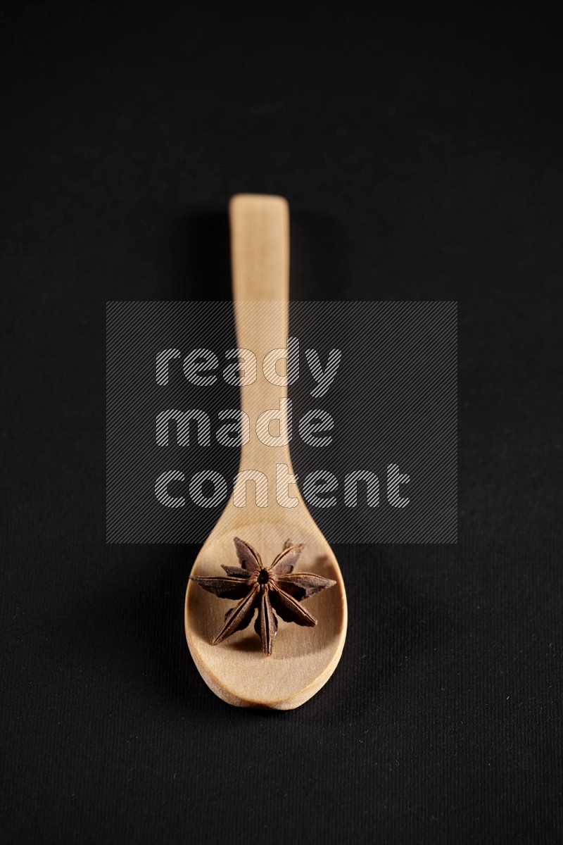 Star Anise in a wooden spoon on more stars anise filling the frame on black flooring