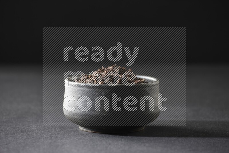 A black pottery bowl full of cloves on a black flooring
