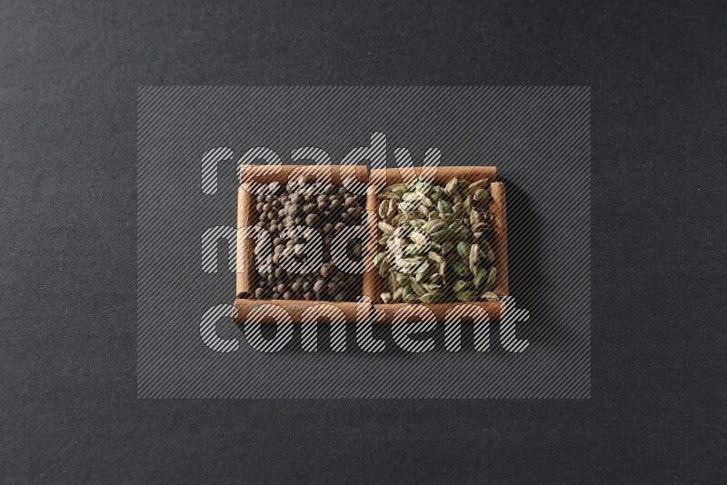 مربعان من أعواد القرفة ممتلئان ببهار الفلفل الحلو وحب الهيل علي خلفية سوداء