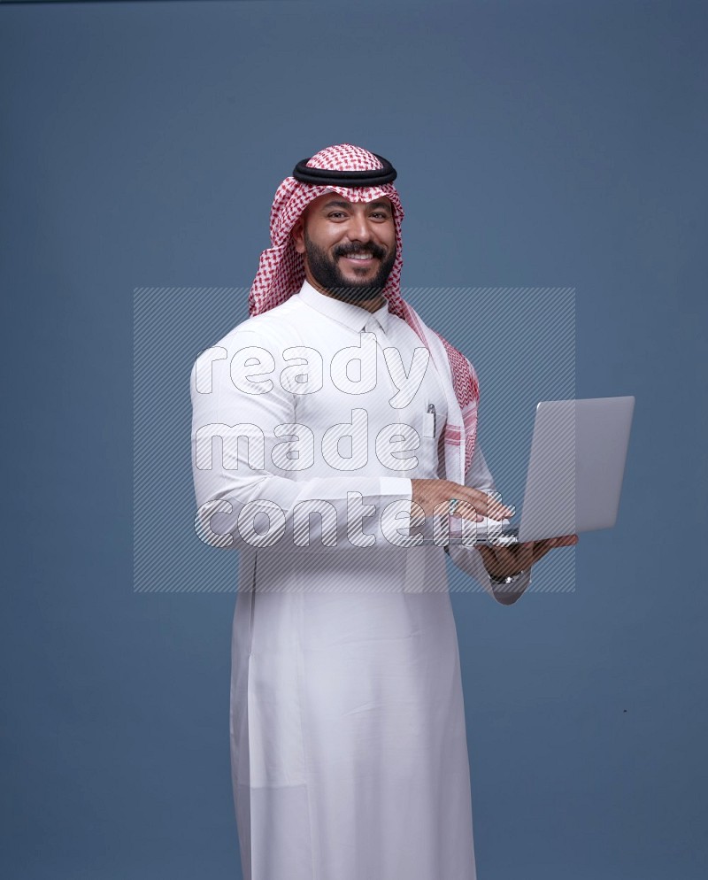 A Saudi man Holding a Laptop on Blue Background wearing Saudi Thob and Shomag