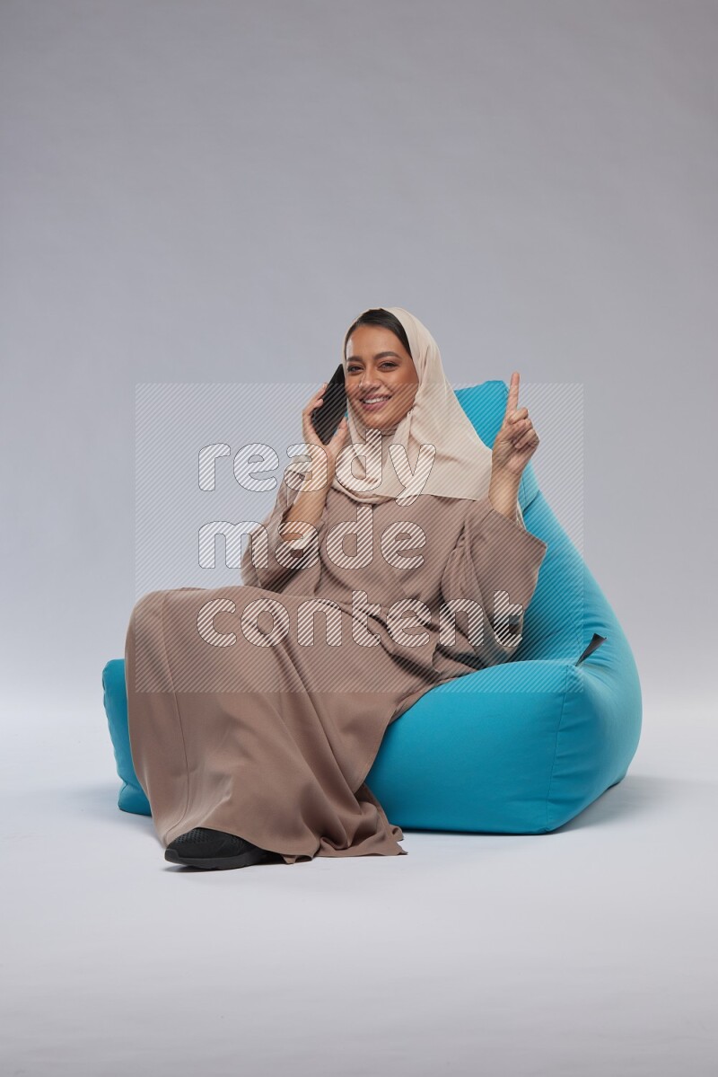 A Saudi woman sitting on a blue beanbag and working on laptop