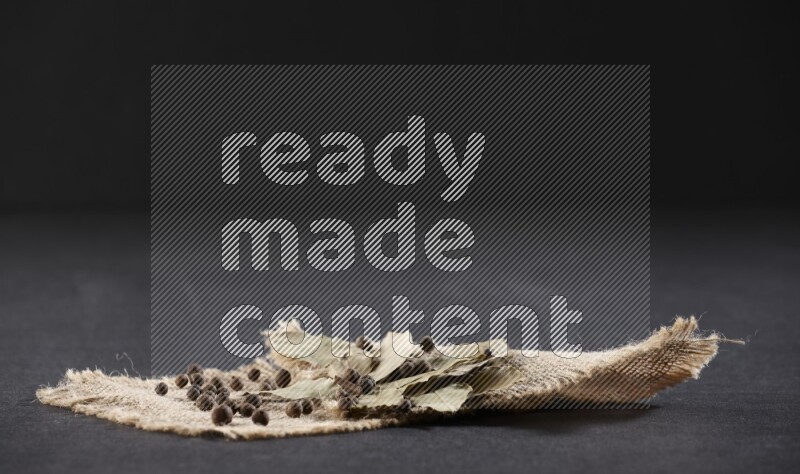 Dried bay leaves and allspice berries on a piece of burlap on black flooring
