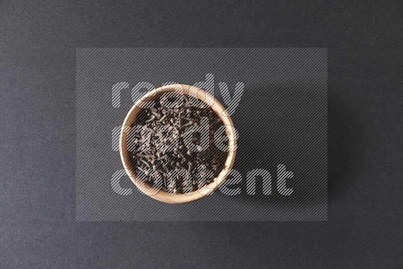 A wooden bowl full of cloves on a black flooring